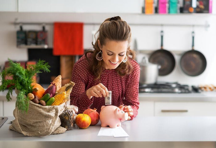 women puts money in piggy bank in her kitchen